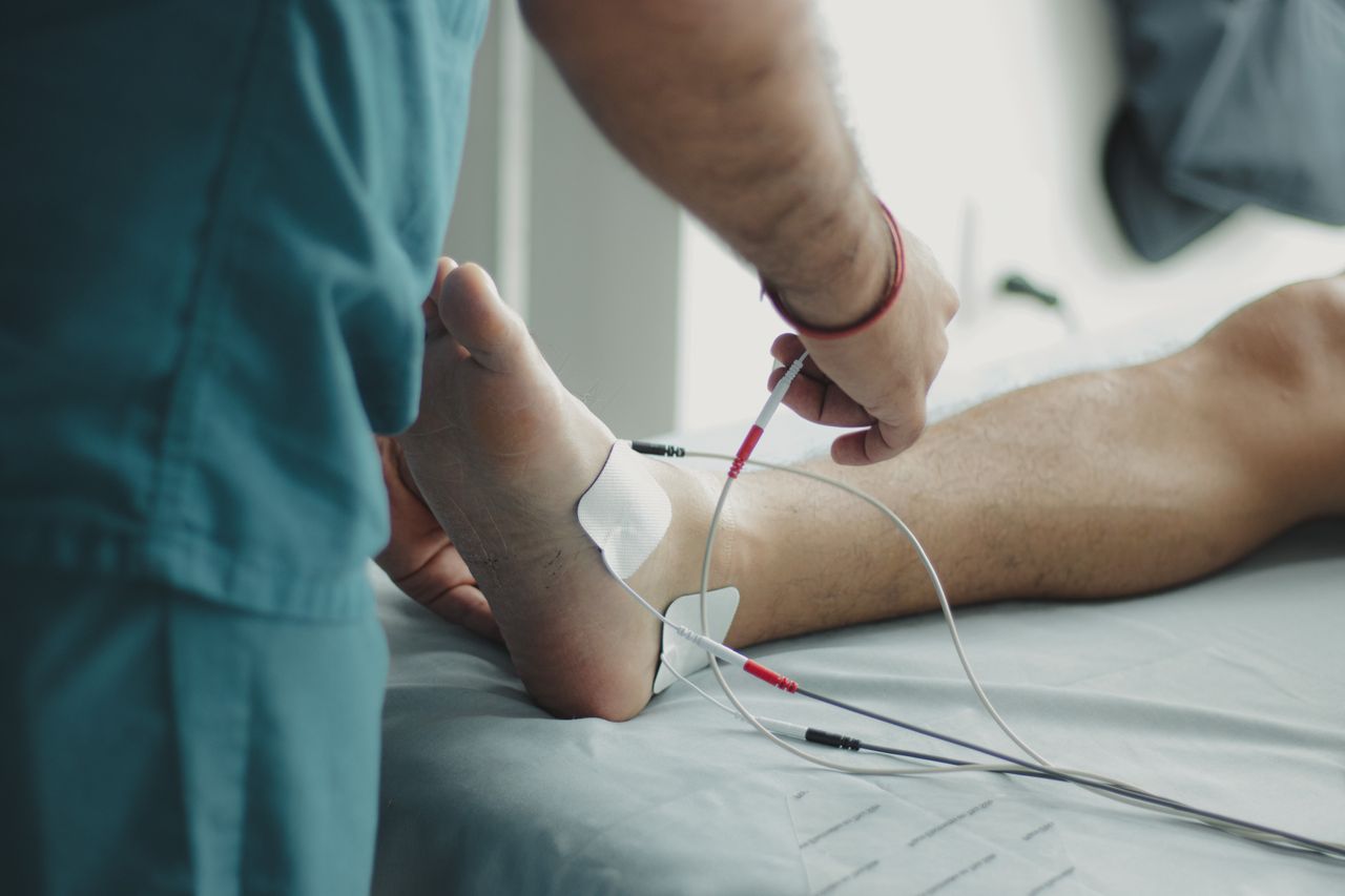 Close-up of a healthcare worker examining a patient's foot with medical equipment in a hospital setting.