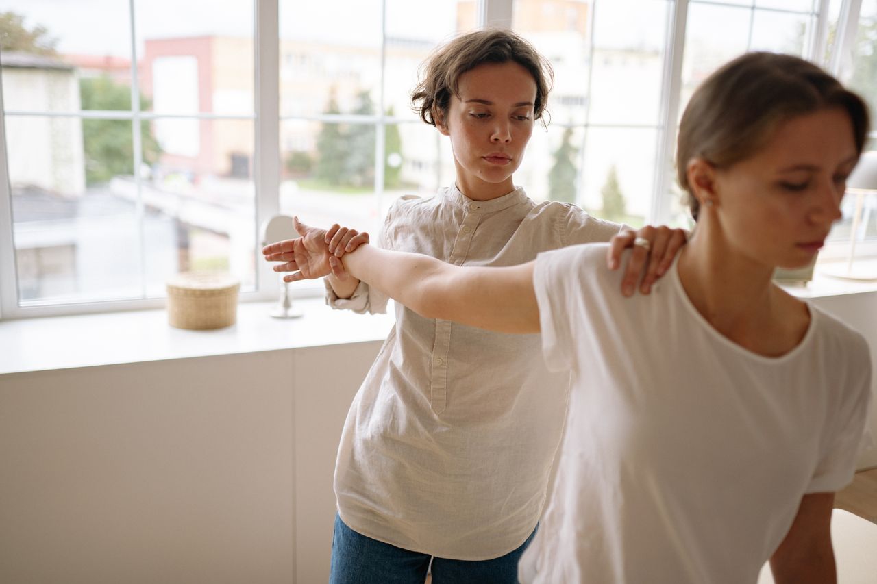 Therapist guiding a client through stretching exercises in a calm indoor setting.